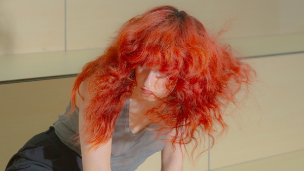 Eine Person mit langen roten Haaren kniet auf einer hölzernen Plattform.