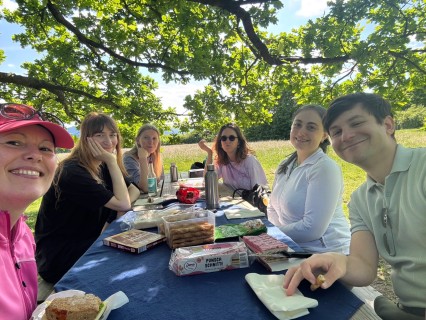 Six people smile at the camera and sit around a picnic table.